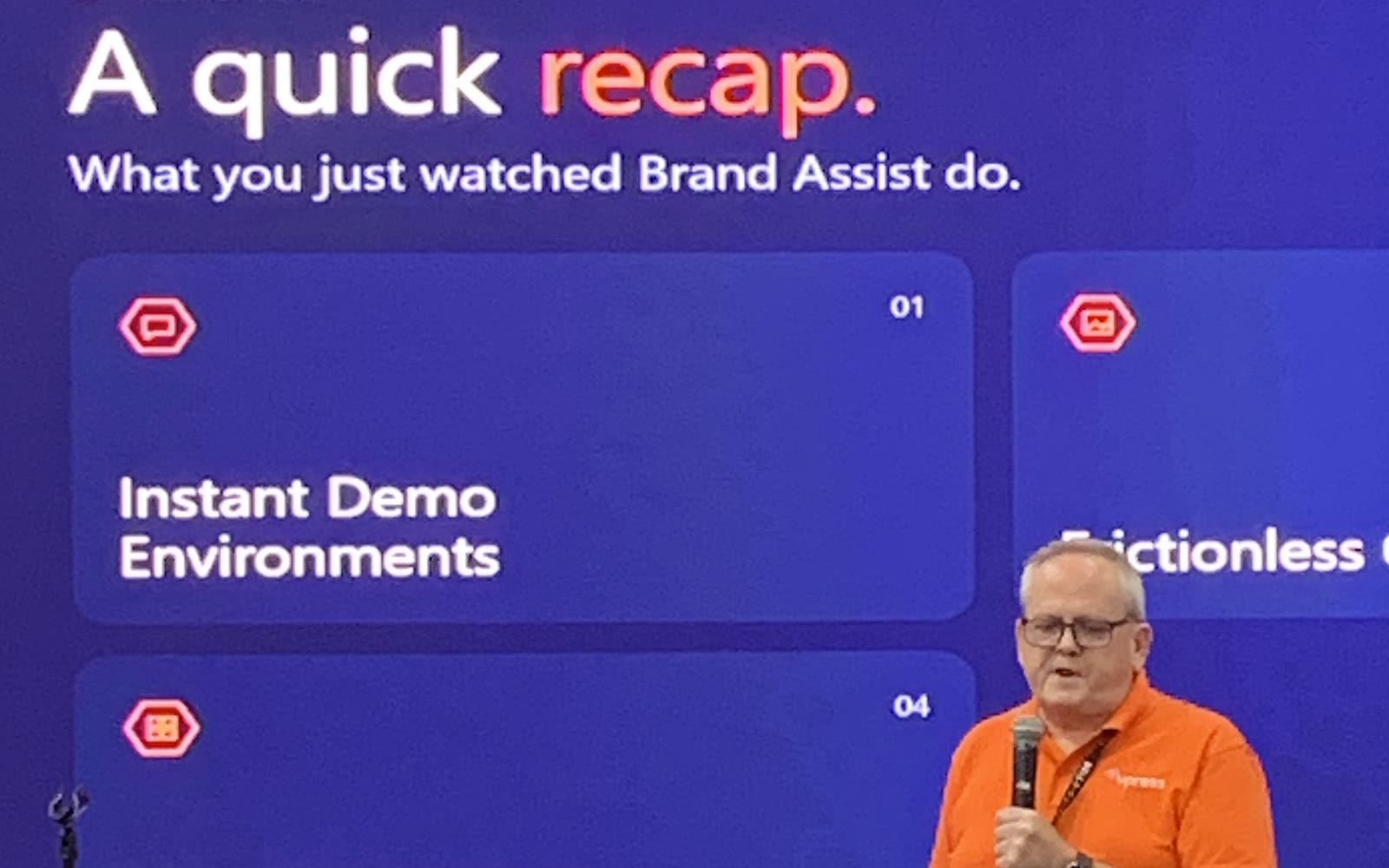 Kelvin Bell on stage at PRINTING United Expo 2026, in front of a slide recapping what Brand Assist does